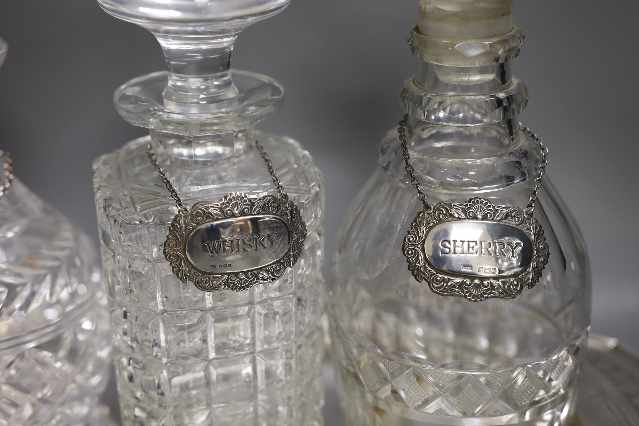 A silver plated oval tray, five assorted cut glass decanters and five assorted silver wine labels.